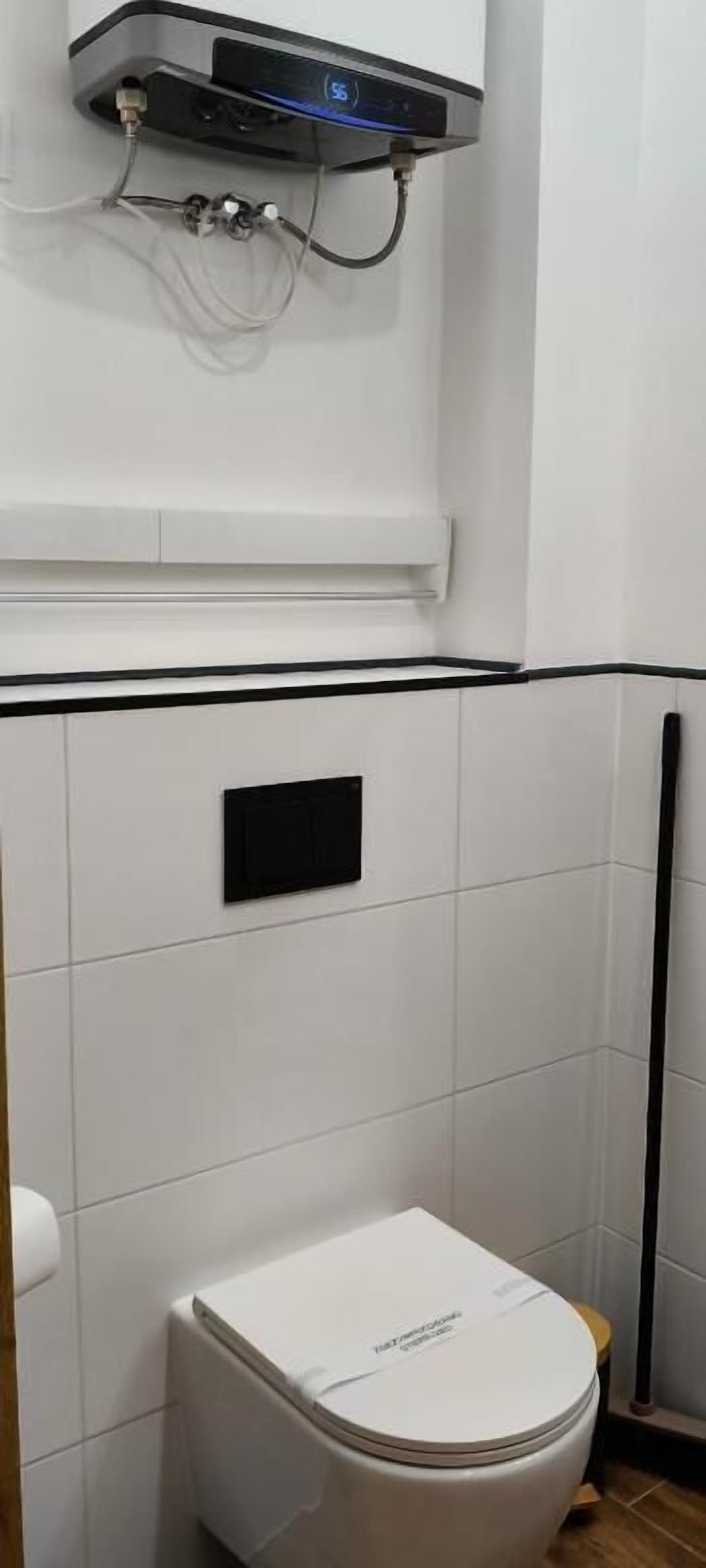 Een badkamer met een toilet, een zwart paneel en een aan de muur bevestigde boiler.