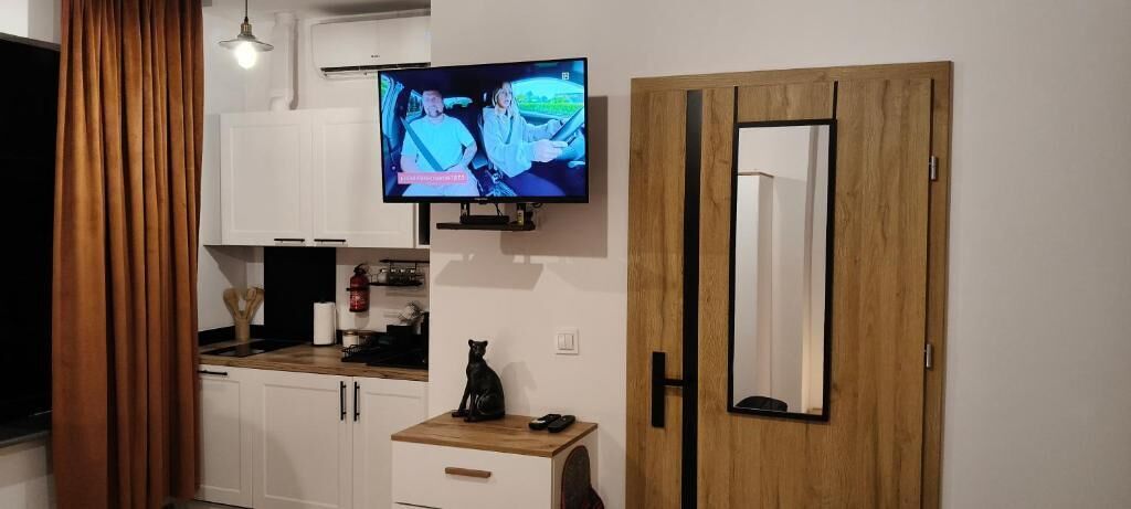 Una cocina moderna con una televisión de pantalla plana sobre la encimera, una puerta de madera con espejo y armarios blancos.