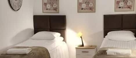 A room with two beds, a round table, a chair, a clock, and wall art.