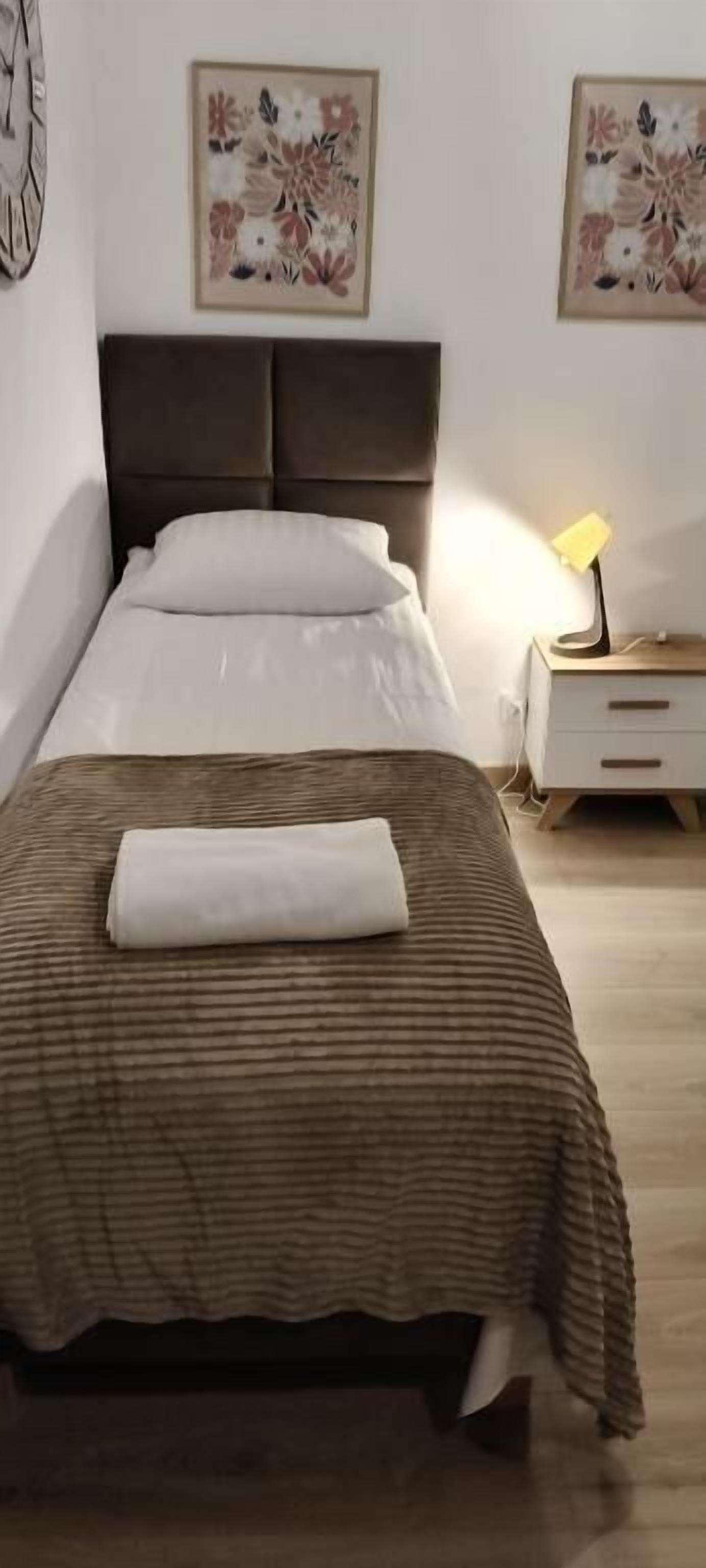 A neatly made bed with a brown striped bedspread and a white pillow, a bedside lamp, and a nightstand with a lamp.
