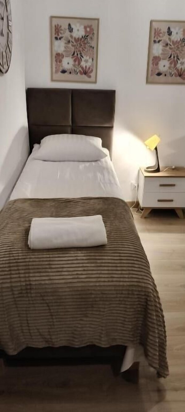 A neatly made bed with a brown striped bedspread and a white pillow, a bedside lamp, and a nightstand with a lamp.