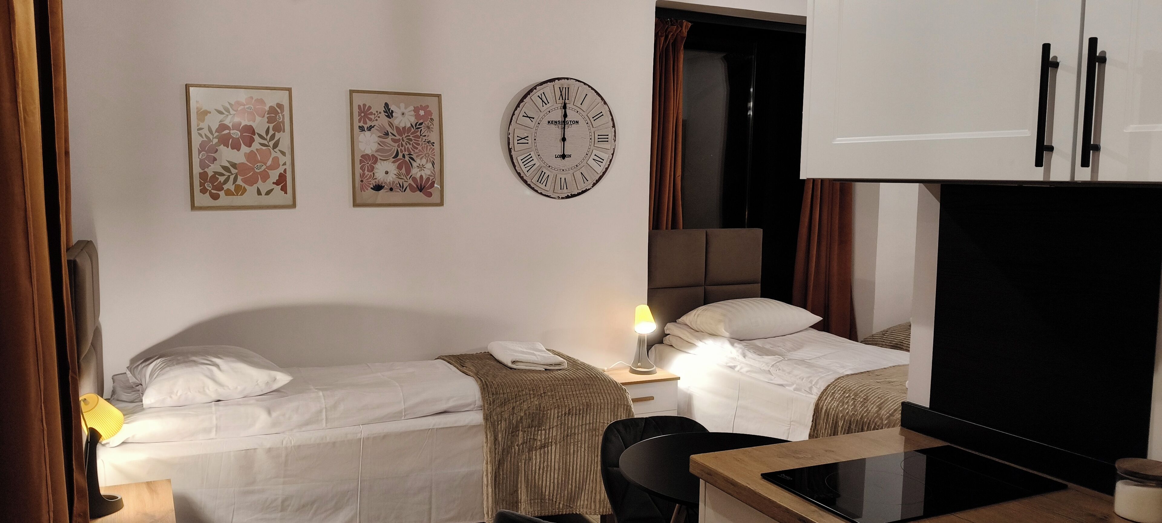 Habitación de hotel con dos camas, un escritorio, una lámpara, un reloj y una televisión.