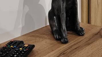 A wooden table with a remote control and a black cat figurine.