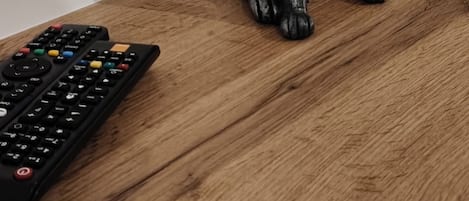 Una mesa de madera con un control remoto y una figurita de un gato negro.