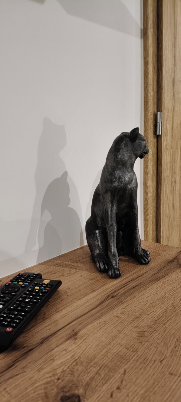 Una mesa de madera con un control remoto y una figurita de un gato negro.
