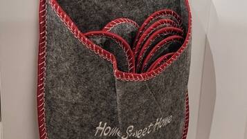 Een grijze opbergmand, bekleed met rood accentleer, met de tekst 'Home Sweet Home' en decoratieve sterren, bevestigd aan een witte kast.
