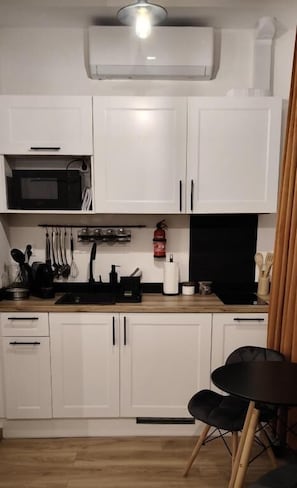 A compact kitchen with white cabinets, a microwave, a sink, and a small dining area with a chair. - Apartamenty Drzewna-Wojska Polskiego (Zielona Góra)