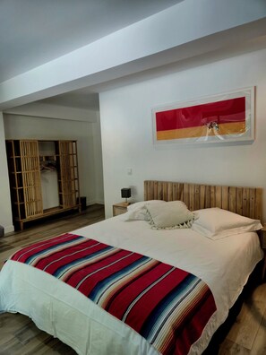 A bedroom with a bed, a wooden headboard, a nightstand, a lamp, a wardrobe, and a painting on the wall.