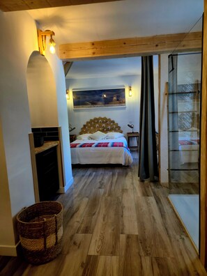 Une chambre à coucher avec une tête de lit en bois, un lit recouvert d’une couverture à rayures, une table de chevet, un tableau accroché au mur et une porte-fenêtre coulissante donnant sur un balcon.