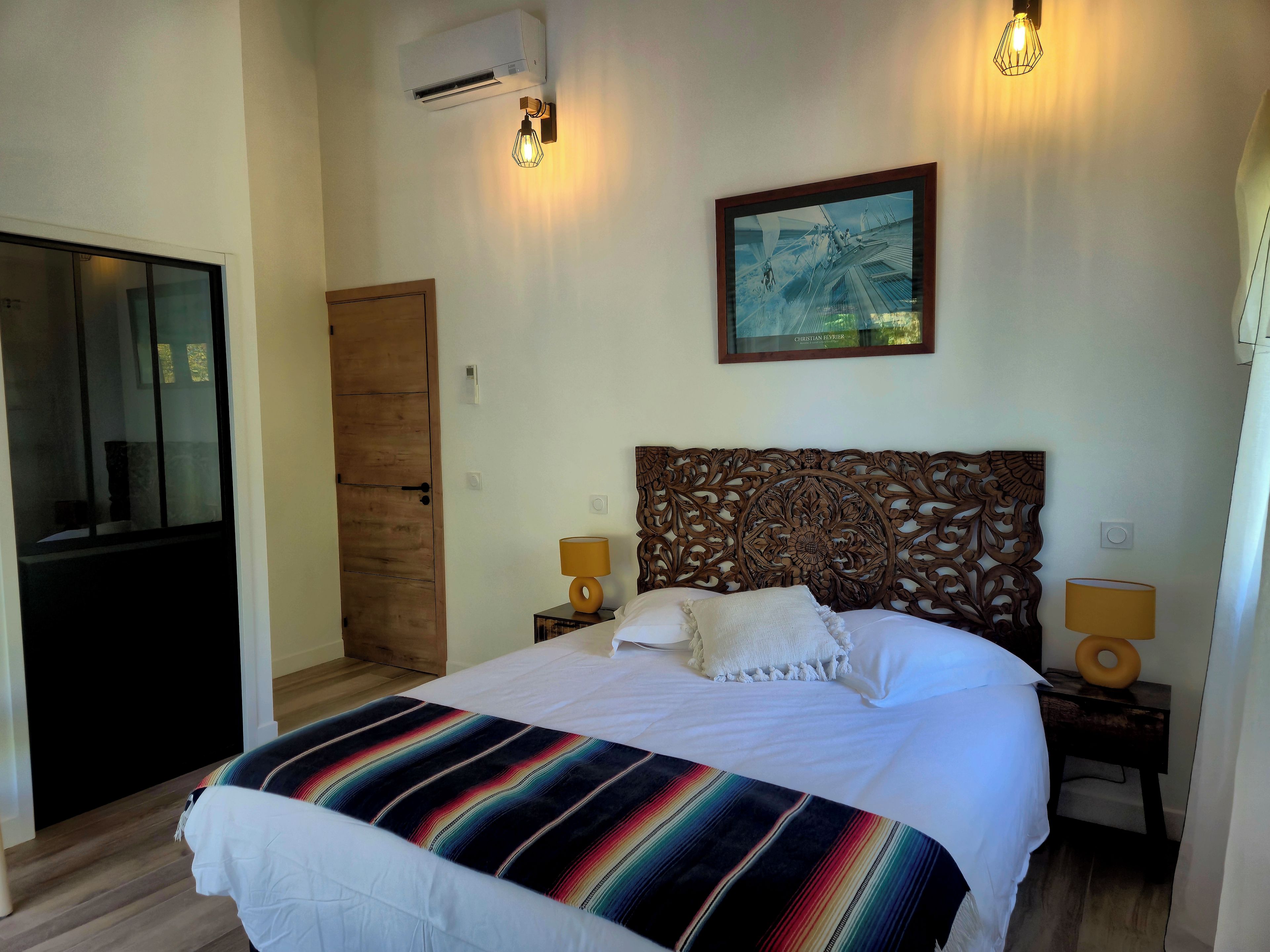 Un dormitorio con una cama grande, una puerta de madera, un cuadro enmarcado en la pared y dos lámparas de noche.