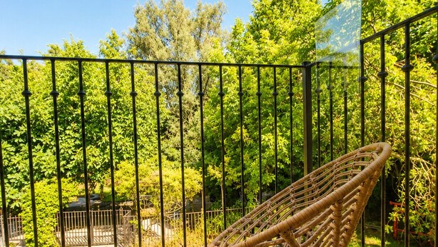 A wooden deck with a wicker chair, surrounded by a metal fence and lush greenery. - Mas La Fontaine de Pernes, les pieds dans la Sorgue, piscine, 12p, 6ch, 5sdb (Pernes-les-Fontaines)