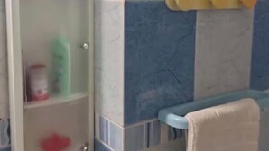A bathroom with a glass cabinet containing toiletries, a towel rack, and a blue-tiled wall.