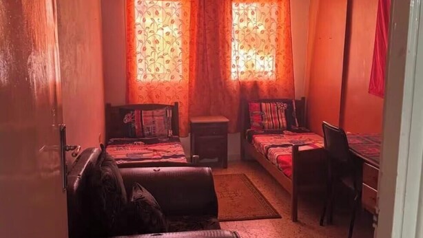 A compact room with a sofa, a small table, and a bed with patterned curtains.