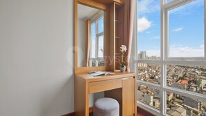 A room with a wooden desk, a mirror, a window with a city view, and a small stool. - Seran by Kozystay  - Taman Sari (West Jakarta)