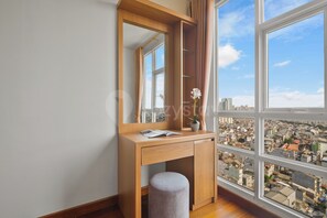 Ein Zimmer mit einem Holztisch, einem Spiegel, einem Fenster mit Stadtblick und einem kleinen Hocker.