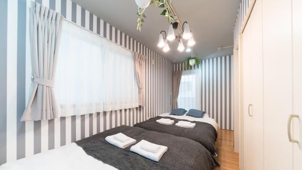 Una habitación de hotel con dos camas, paredes a rayas, un candelabro y una planta.