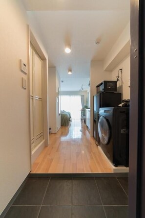 A hallway with a wooden floor, a washing machine, and a door on the left.