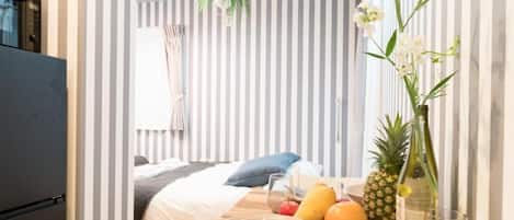 A hotel room with a bed, a breakfast table with fruits and a bottle, and a plant.