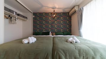 Une chambre avec deux lits, un mur décoré d’un motif, une étagère avec des boîtes de rangement et un luminaire suspendu.