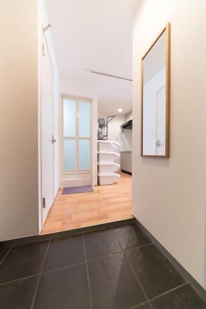 A narrow hallway with a wooden floor leading to a room with a bed and a window.