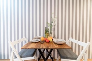 A dining table with a wooden top, surrounded by white chairs with grey cushions, set against a striped wallpaper background.