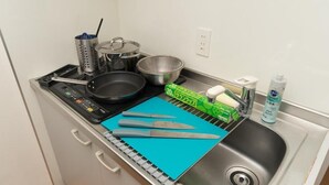 Una kitchenette equipada con estufa, ollas, sartén, tabla de cortar y lavamanos.
