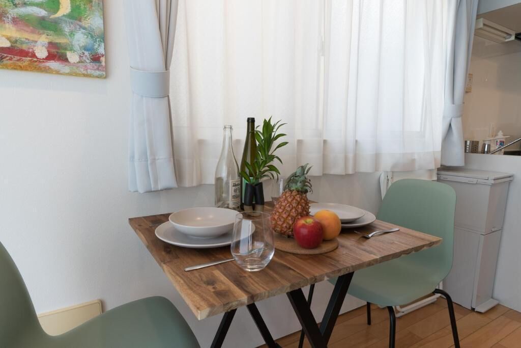Een eetgedeelte met een houten tafel, stoelen, een schaal, een wijnglas en een schaal met fruit.