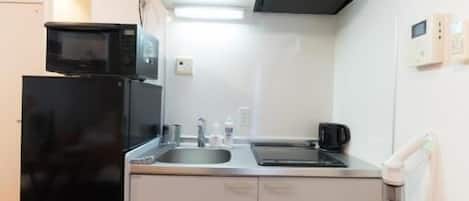 A compact kitchen with a black refrigerator, a microwave, a stove, and a sink.