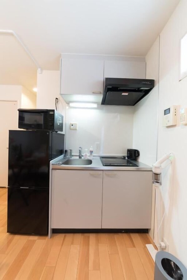 A compact kitchen with a black refrigerator, a microwave, a stove, and a sink.