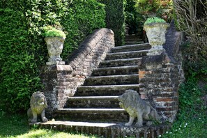 A stone staircase with a brick handrail, flanked by two stone lion statues, leading up to a hedge.