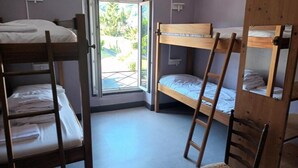 Un dormitorio con literas, una silla de madera y una ventana con vistas a la vegetación.