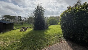 Un patio cubierto de césped con un cobertizo de madera, un árbol y un seto.