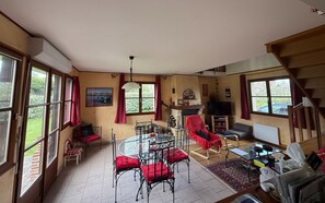 A spacious living room with a fireplace, a dining area with a glass table, and a staircase leading to an upper level. - Les Buissons (st pierre le vieux)