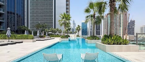 A swimming pool with lounge chairs, surrounded by palm trees and modern buildings.
