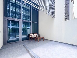 Un bâtiment moderne avec une entrée dotée d’une porte en verre, un petit espace détente avec deux chaises et une table, et un sol carrelé.