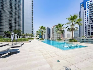 A rooftop pool area with lounge chairs and umbrellas, surrounded by high-rise buildings. - Chic 1BR Duplex in The Sterling | Business Bay (Dubai)