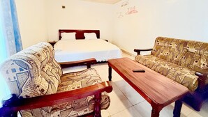 A room with a bed, two patterned sofas, a wooden table, and a wall with a light fixture. - SKY LIGHT VILLA (Kigali)