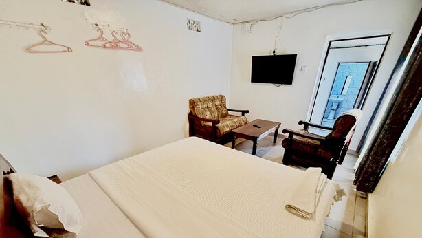 A hotel room with a bed, two chairs, a small table, and a TV mounted on the wall. - SKY LIGHT VILLA (Kigali)