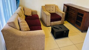 A living room with a sofa, armchair, and a small black table with a remote control. - SKY LIGHT VILLA (Kigali)
