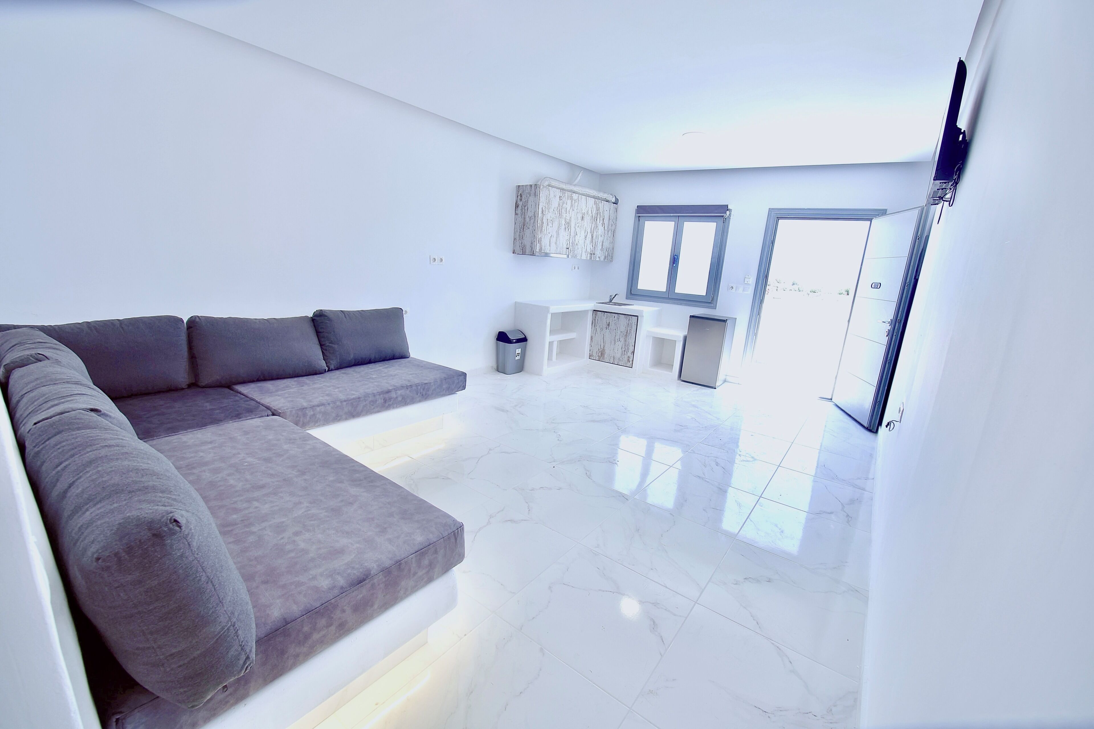 A modern living room with a sectional sofa, a dining area with a small table and chairs, and a kitchen area with cabinets and a sink.