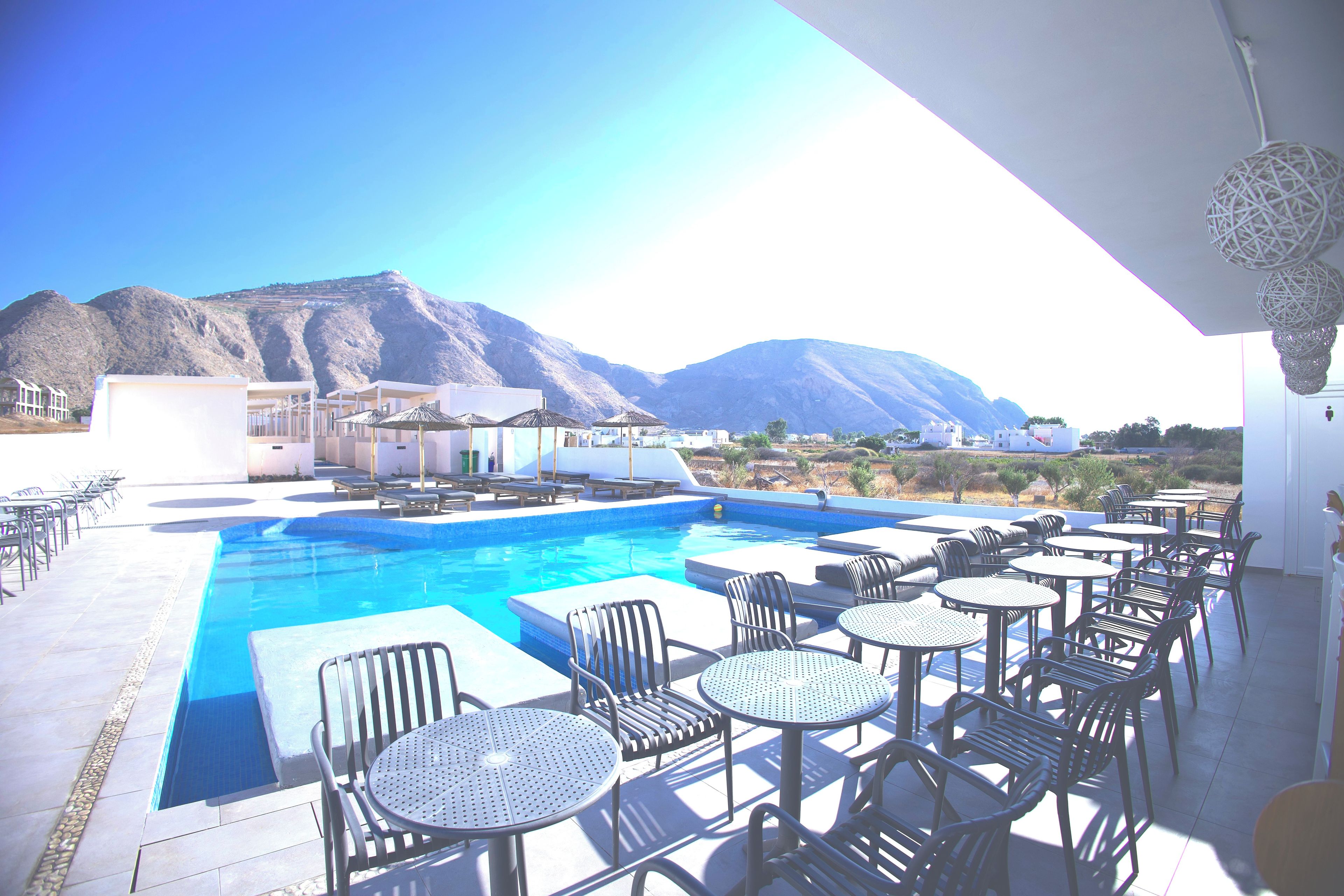 A pool area with lounge chairs and tables, a clear view of mountains in the background, and a modern architectural style.