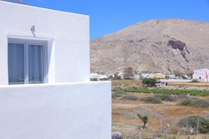 A white building with a window, a mountainous landscape, and a small settlement in the background. - Tinamar Selection (Santorini)