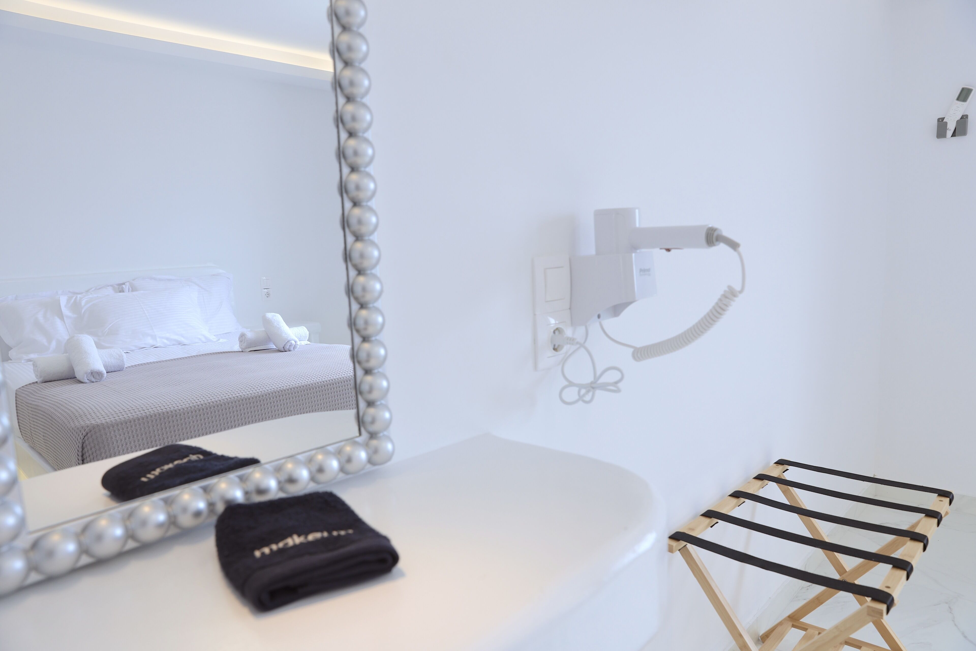A hotel room with a bed, a mirror with a pearl frame, a towel, and a hairdryer on the wall.
