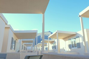 A series of modern, white buildings with balconies, arranged in a linear fashion, overlooking a mountainous landscape. - Tinamar Selection (Santorini)