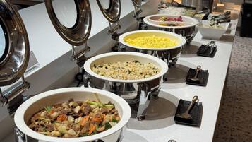 Un bufé con múltiples recipientes de comida al servicio, incluyendo platos de arroz y verduras salteadas.
