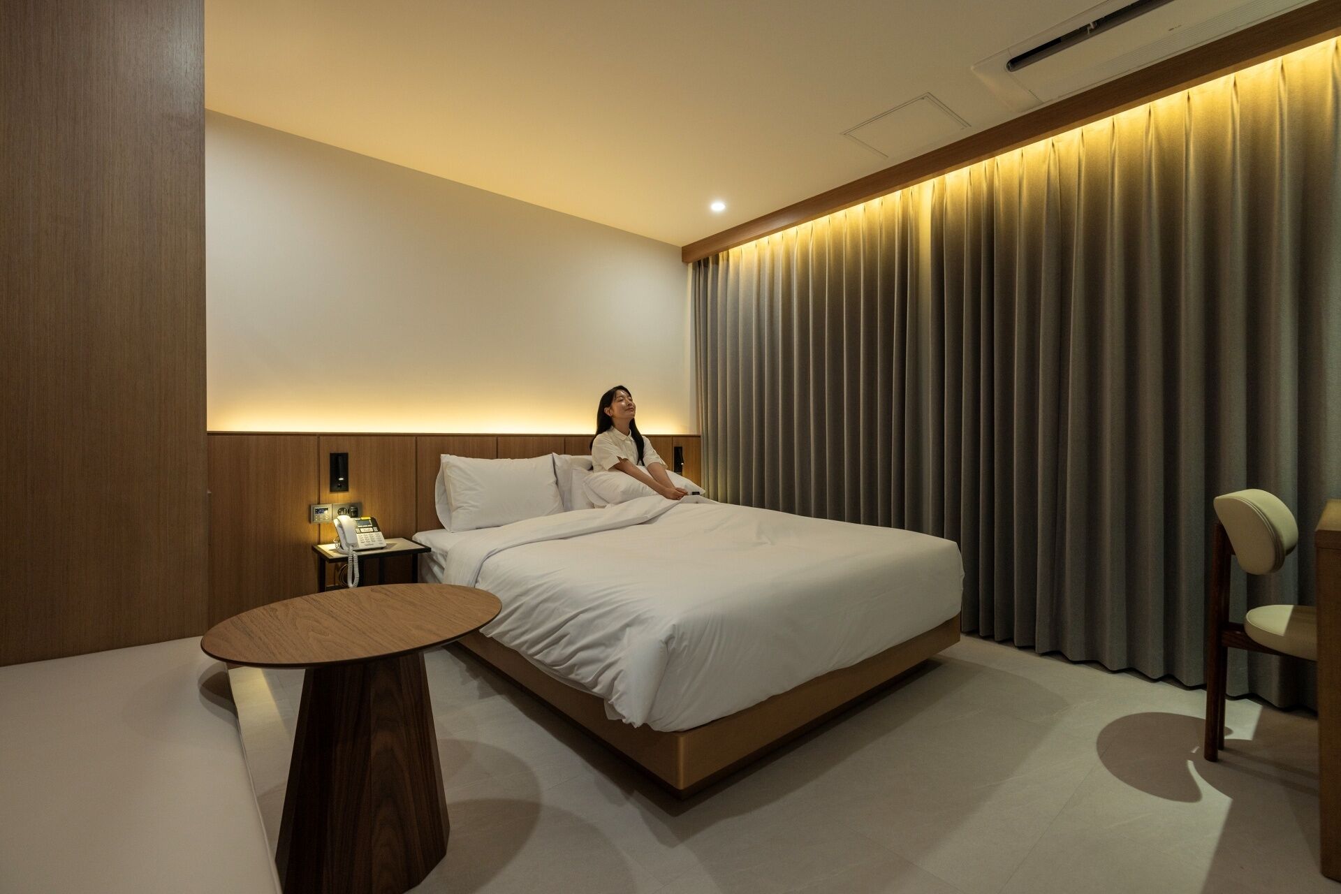 A hotel room with a large bed, bedside table, and a chair.