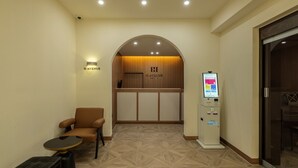 Ein Hotel-Empfangsbereich mit Empfangsschalter, einer Sitzecke inklusive Stuhl und Tisch sowie einem Self-Service-Terminal.
