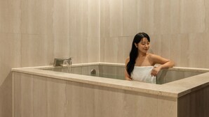 Eine Person liegt in einer Badewanne mit einem Handtuch, umgeben von gefliesten Wänden.