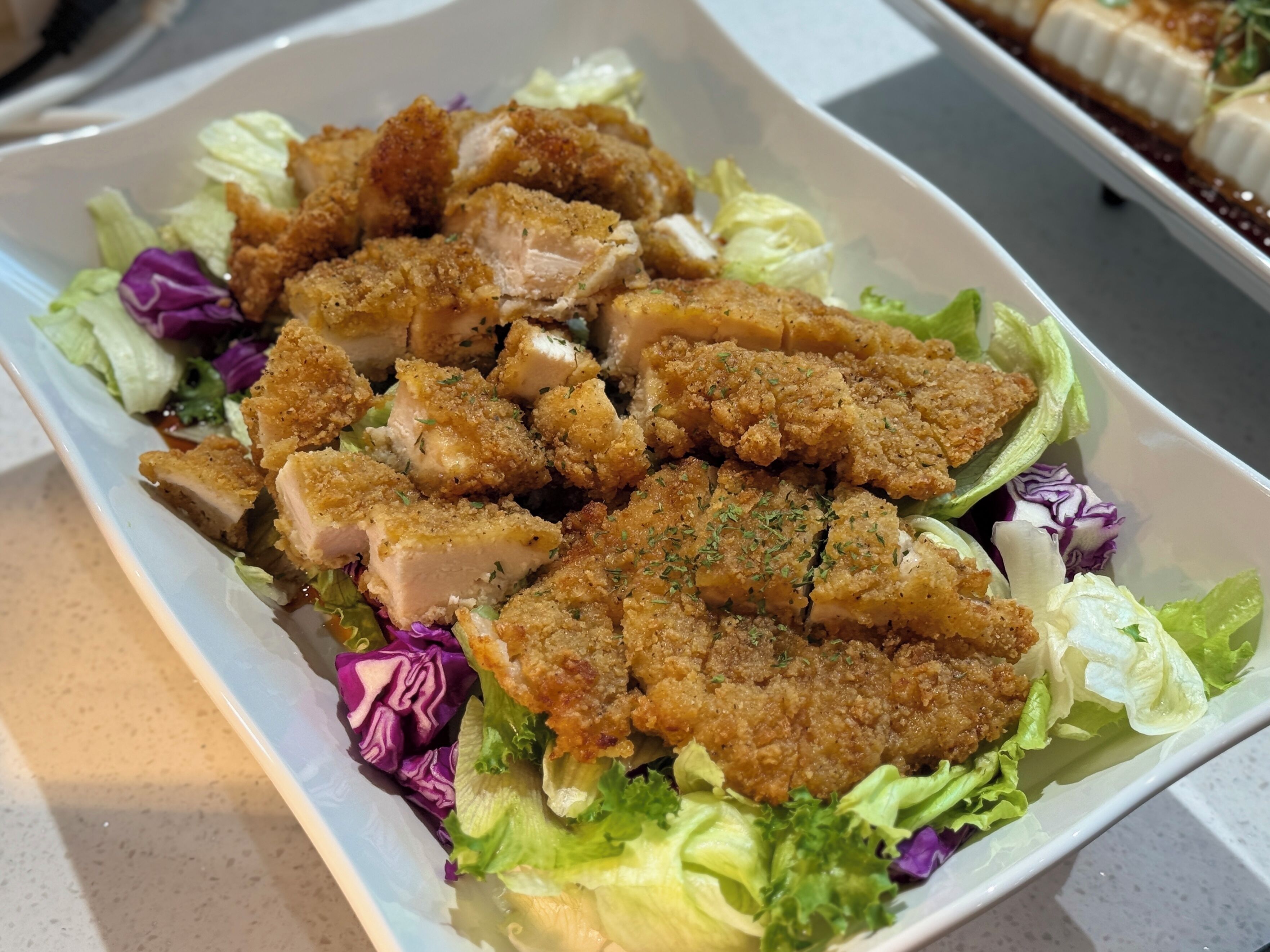 A rectangular white plate with a salad containing lettuce, purple cabbage, and breaded chicken pieces.