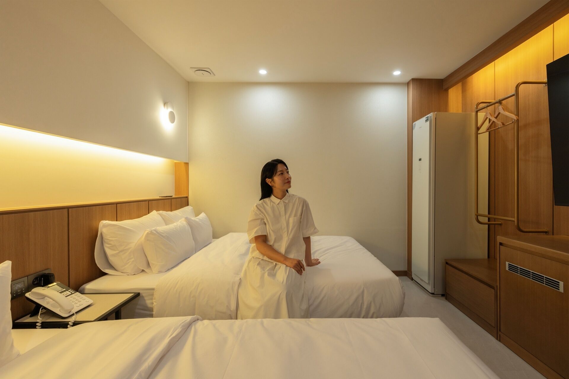 A hotel room with two beds, a bedside telephone, a wardrobe, and a mirror.